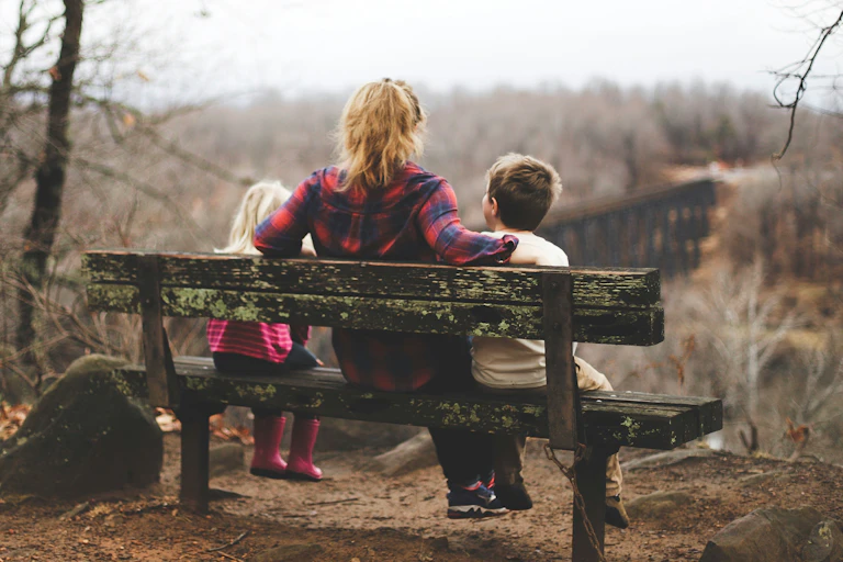 Mother sits with two children on outside bench seat