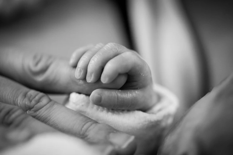 Black and white photo of a baby's hand holding an adult's finger
