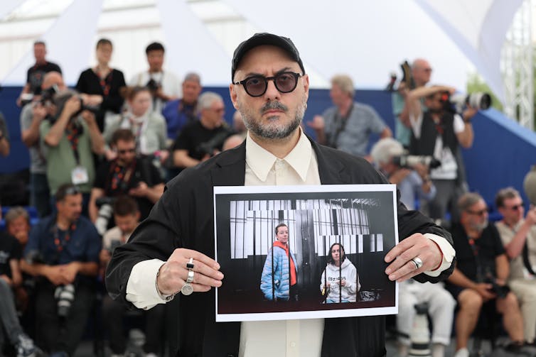 Russian director Kirill Serebrennikov holds a picture of Berkovich and Petriychuk on the red carpet.