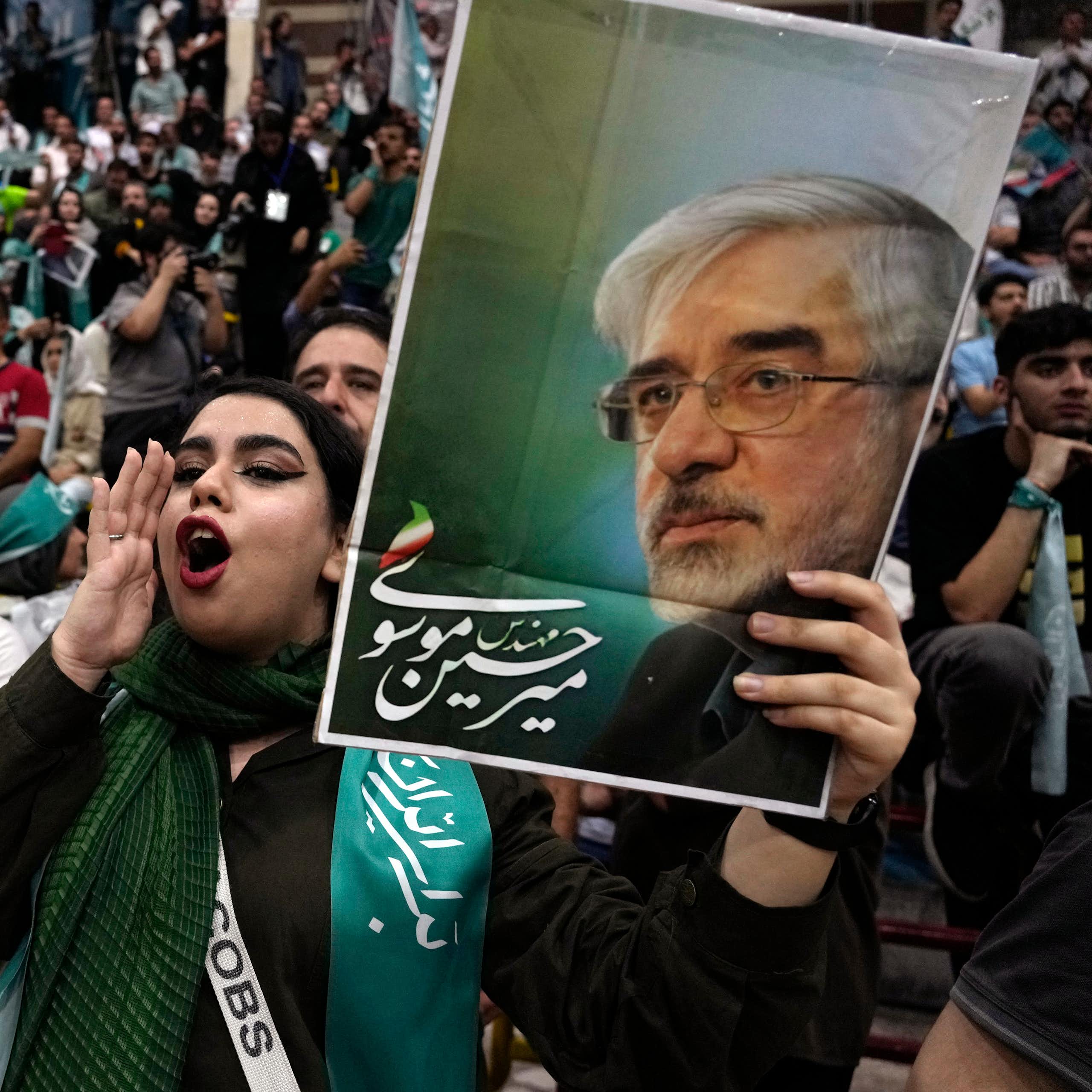 A large crowd of Iranian supporters of Masoud Pezeshkian gather in Tehran; in the foreground, a young woman shouts her endorsement while holding up a campaign sign.