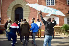 Community members outside a court waving a giant fish made out of paper and dancing in celebration