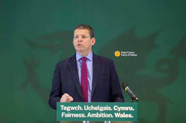 Rhun ap Iorwerth on stage in front of a screen with a green dragon