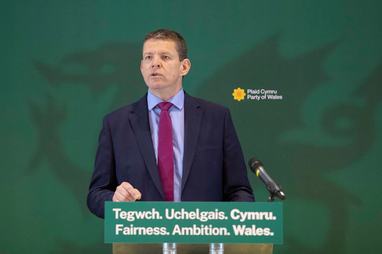Rhun ap Iorwerth on stage in front of a screen with a green dragon