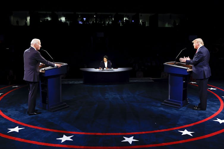 Two men on a stage face a moderator.