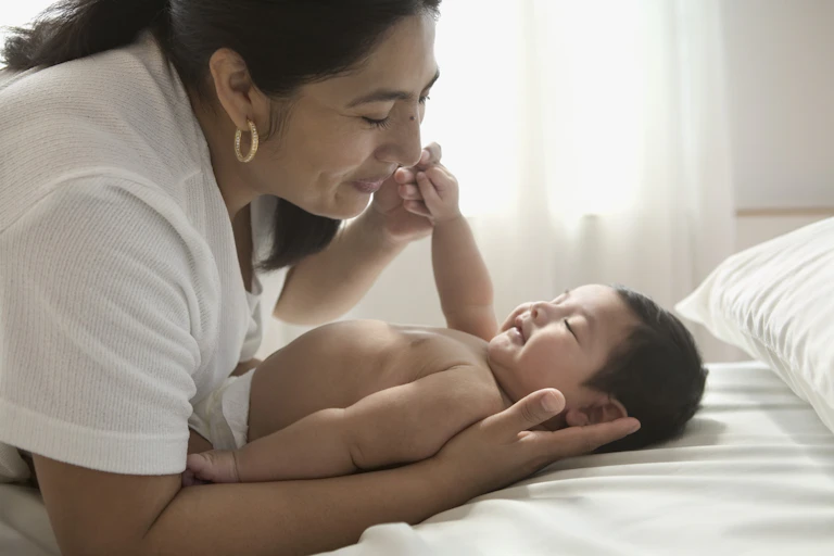 Mother smiles at and caresses infant lying on bed