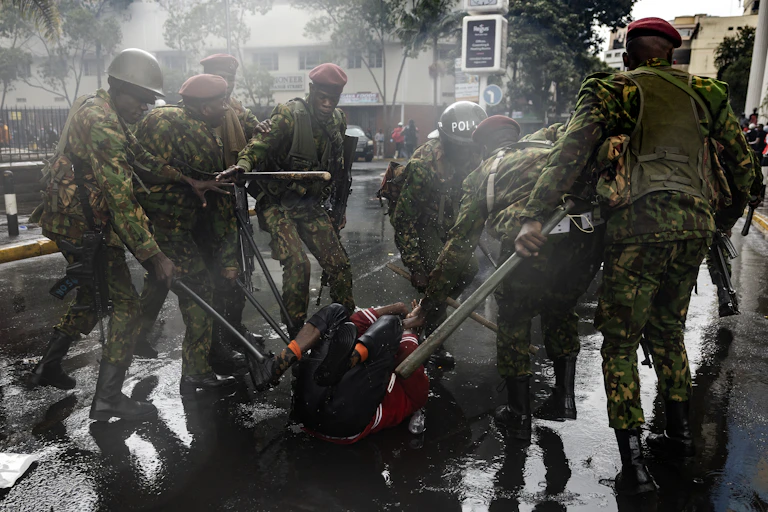 Men dressed in army fatigues and holding batons surround and beat a man lying on the ground