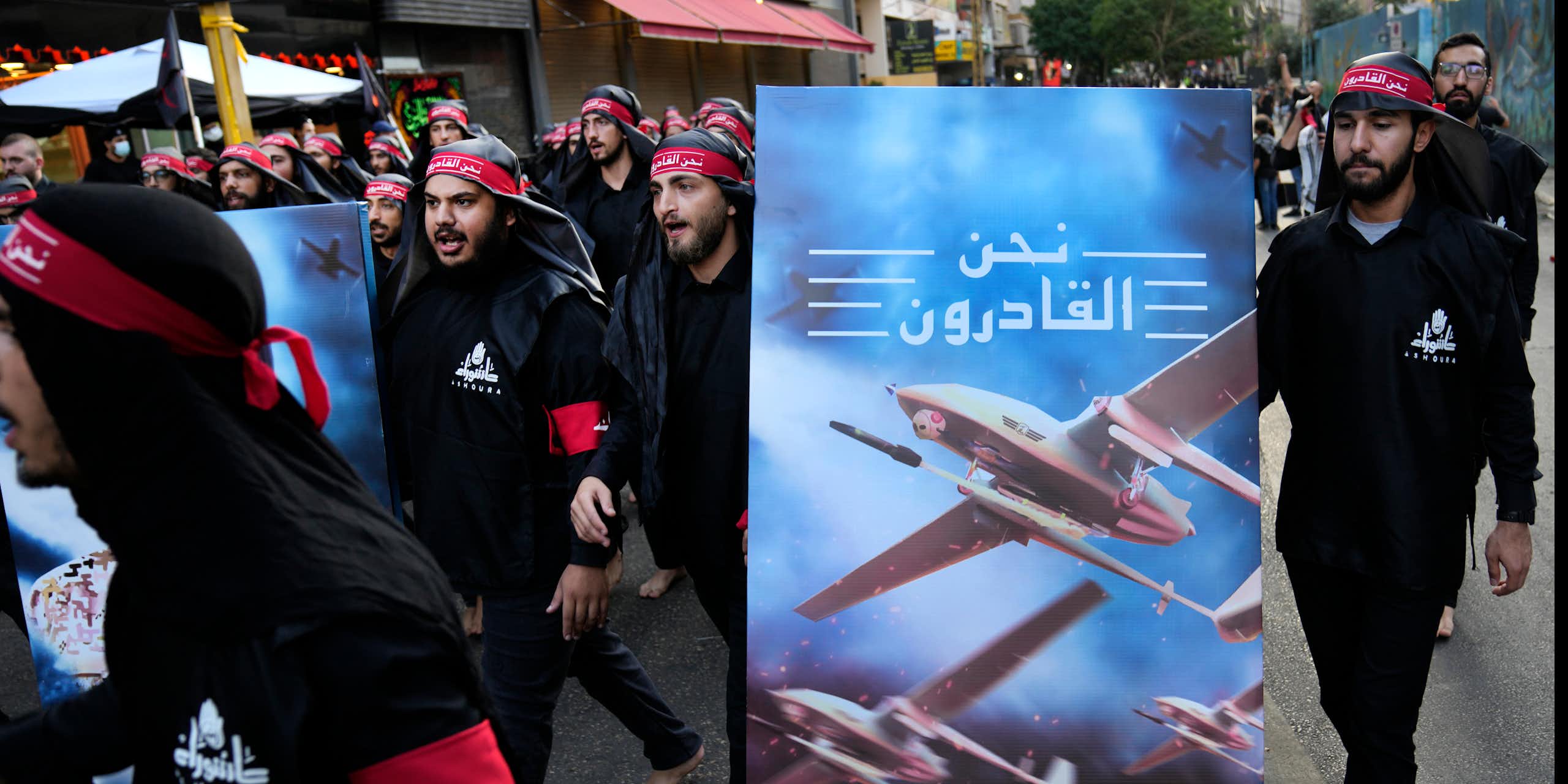 Men dressed in black wearing red headbands walking with a poster featuring a drone and Arabic writing