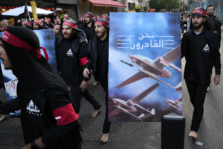 Men dressed in black wearing red headbands walking with a poster featuring a drone and Arabic writing