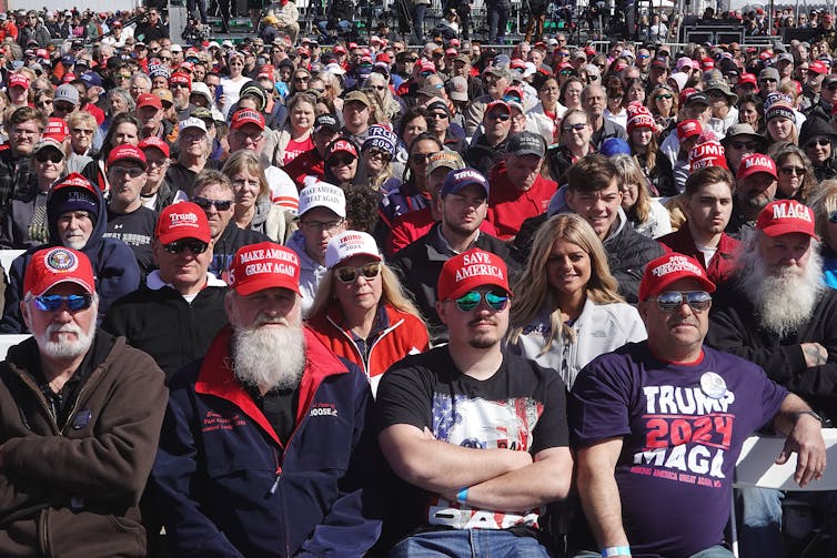 A large crowd of people face forward and wear red hats that say 'Make America Great Again.'