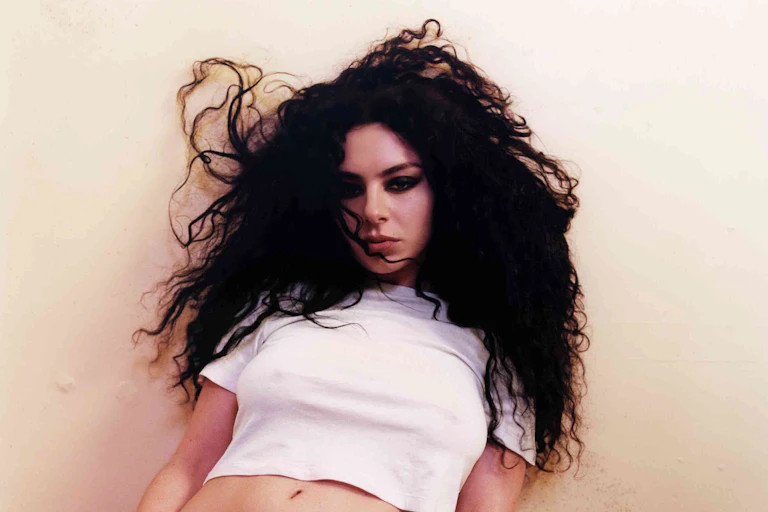 Charli leaning against a wall in a white crop top