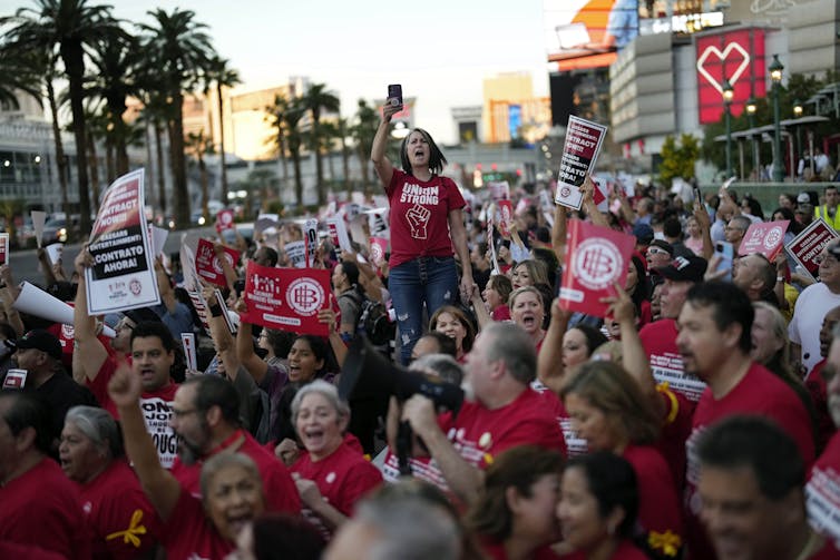 A group of people in red shirts wave signs and yell.