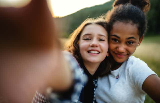 two teenage girls smile as they stand cheek to cheek
