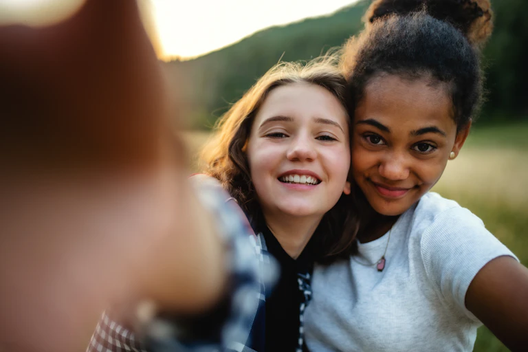 two teenage girls smile as they stand cheek to cheek