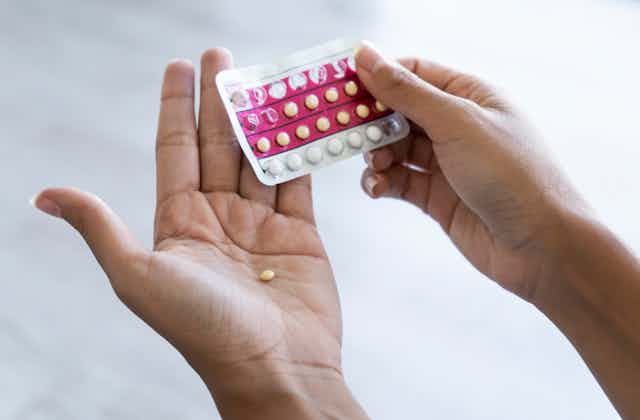 Close de uma pessoa segurando um blister de pílulas anticoncepcionais, com uma pílula na palma da mão