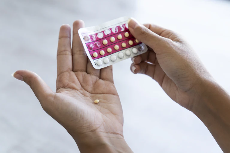 Close de uma pessoa segurando um blister de pílulas anticoncepcionais, com uma pílula na palma da mão