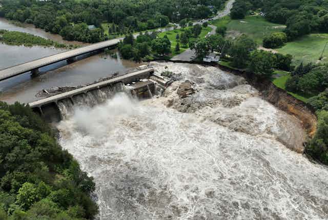 Water pours through a dam and flows around one side of the structure.