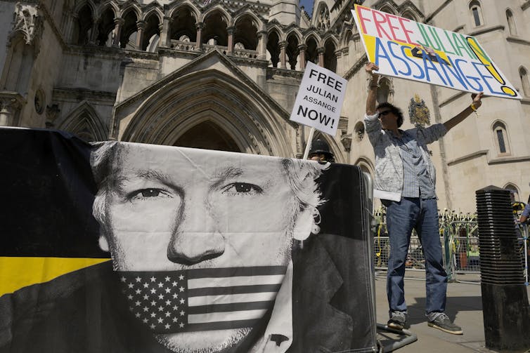 A poster of Julian Assange with the American flag over his mouth outside a historic building