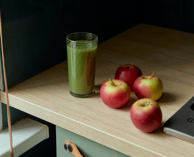 glass of green juice on benchtop with red apples
