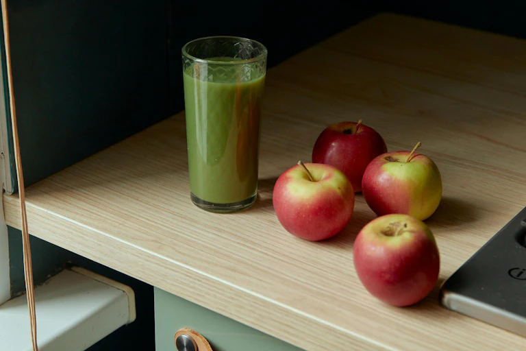 glass of green juice on benchtop with red apples