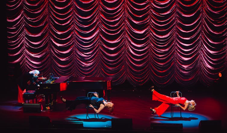 One woman at a piano, two women lie on chairs.