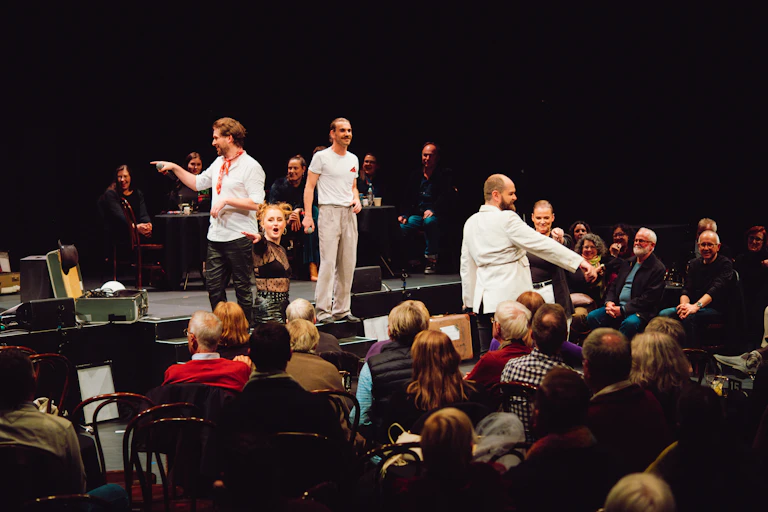 Actors stand among an audience.