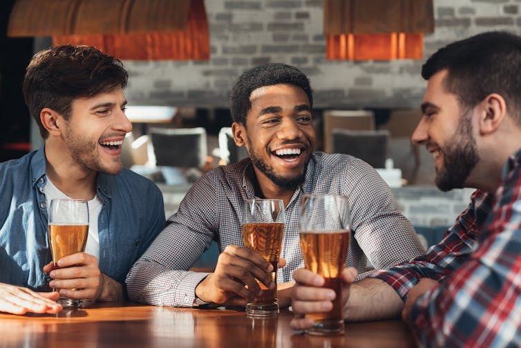 Três homens sorrindo e conversando em torno de uma mesa em um pub