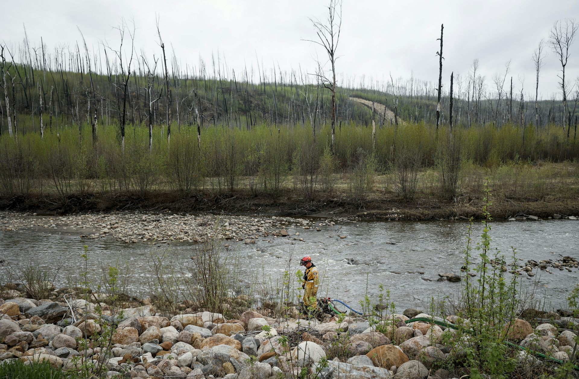 A firefighter seen with a hose against a burnt out landscape.