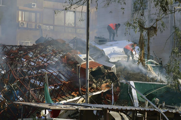 Two men search through rubble.