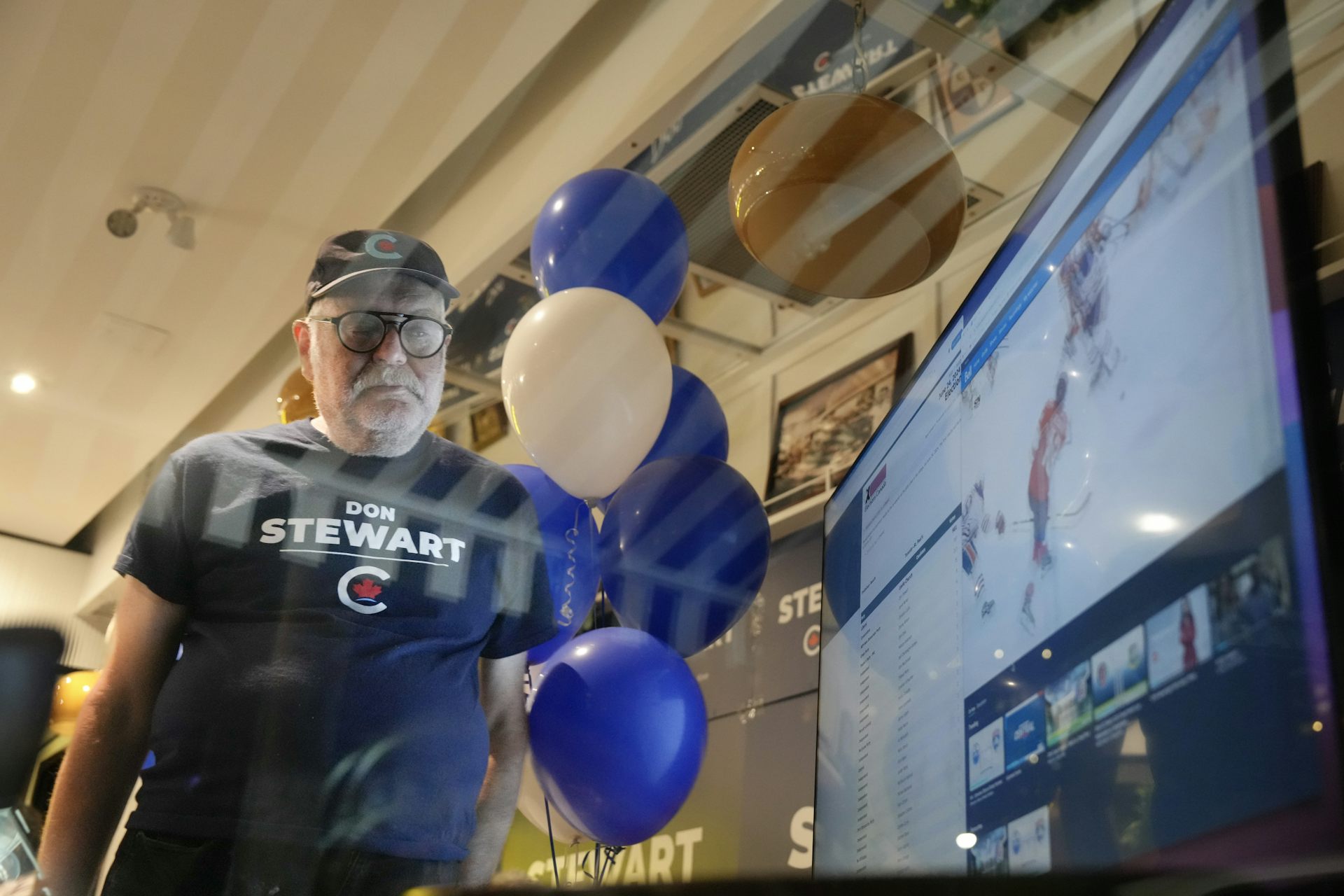 A man wearing a blue Don Stewart T-shirt stares at the TV screen.