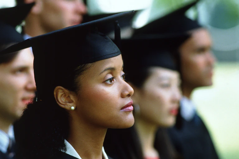 A woman with a look of uncertainty wears a black graduation cap.