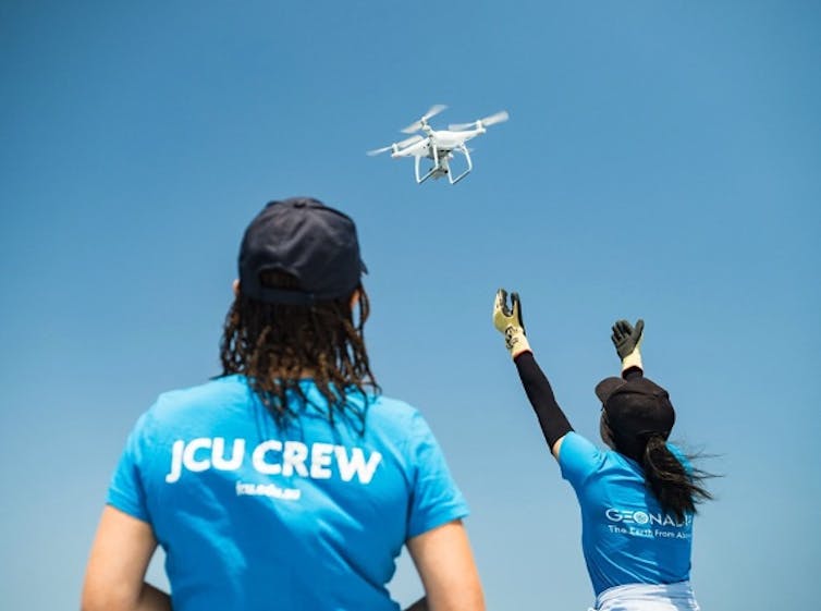 Two women in blue shorts watch a drone