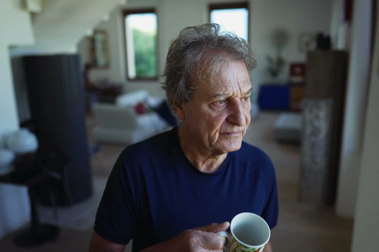 older man stands near window looking downcast