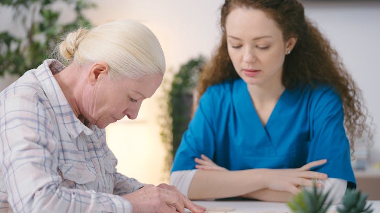 older woman looks down at table while carer looks on