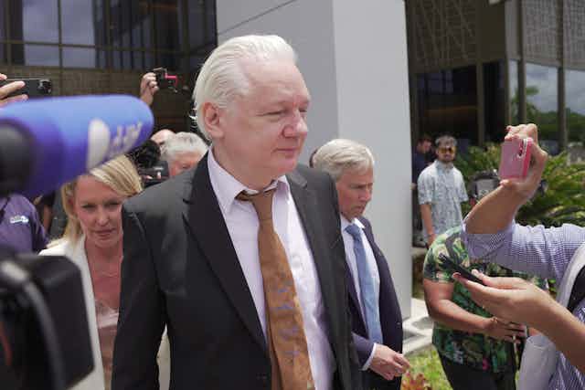A man in a suit walks out of a court surrounded by cameras and people