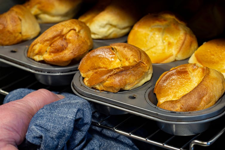 person pulls tray of golden baked puddings out of oven