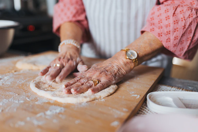 older woman's hands making pizza dough on floured board