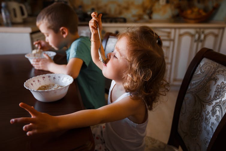 two young children at dinner table enjoying bowls of food with spoons