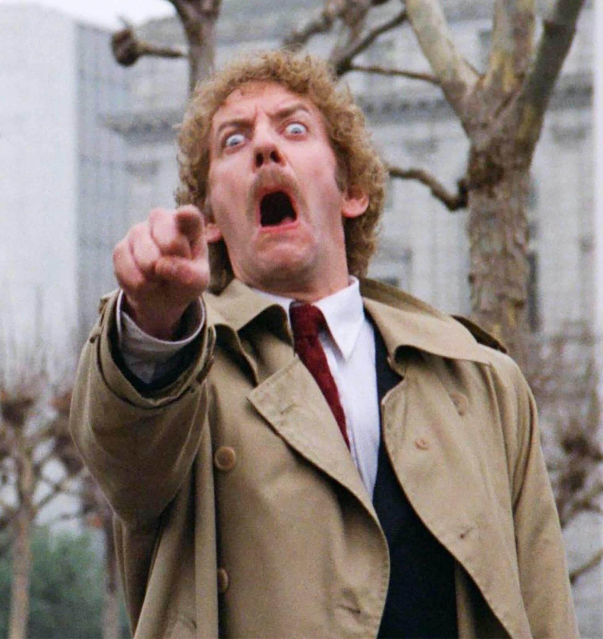 A man dressed in a mac with a horrified and distressed look on his face.