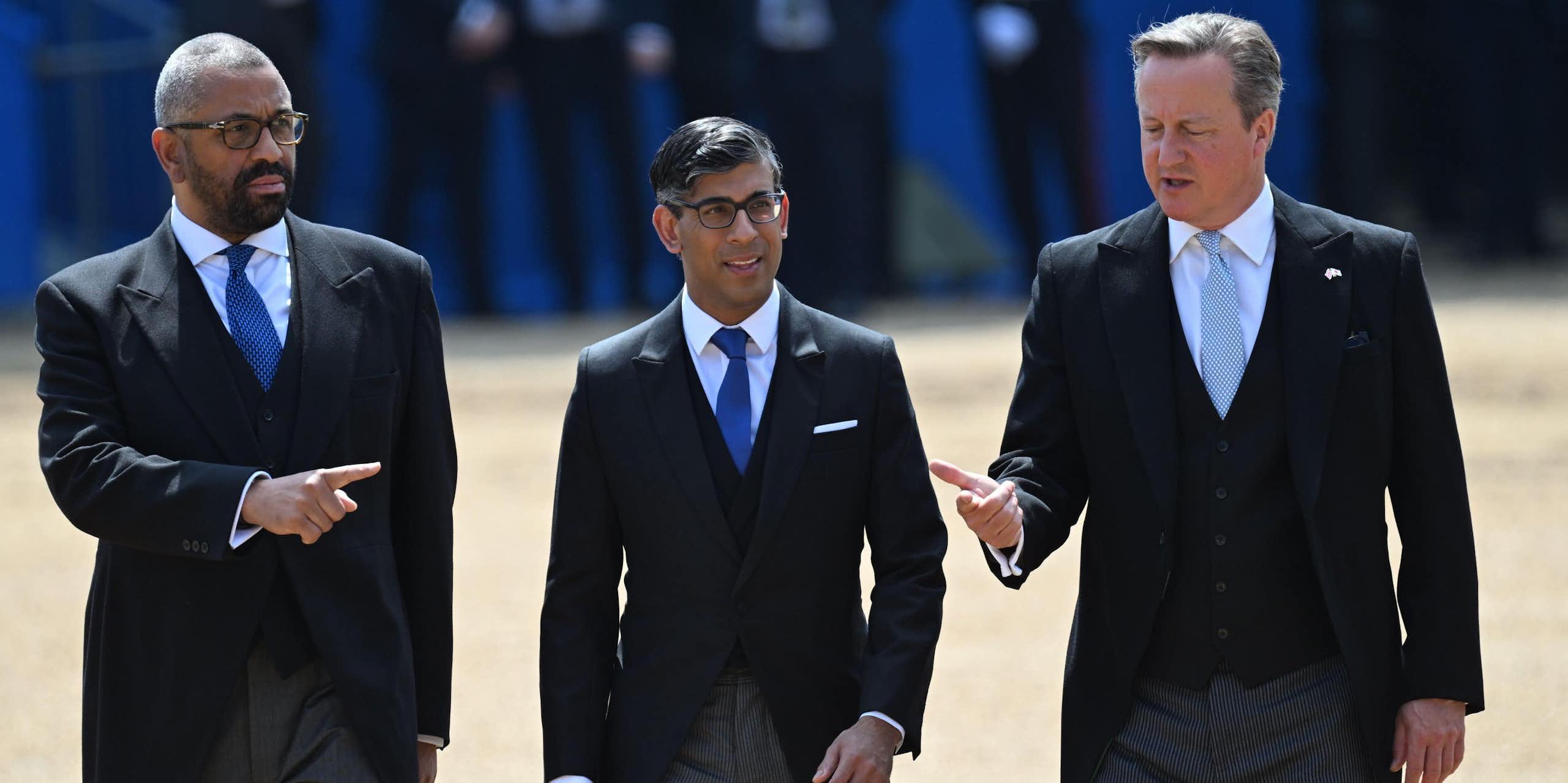 James Cleverly, Rishi Sunak and David Cameron walking together, with Cleverly pointing in one direction and Cameron the other, both towards Sunak.