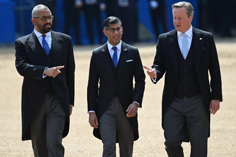 James Cleverly, Rishi Sunak and David Cameron walking together, with Cleverly pointing in one direction and Cameron the other, both towards Sunak.