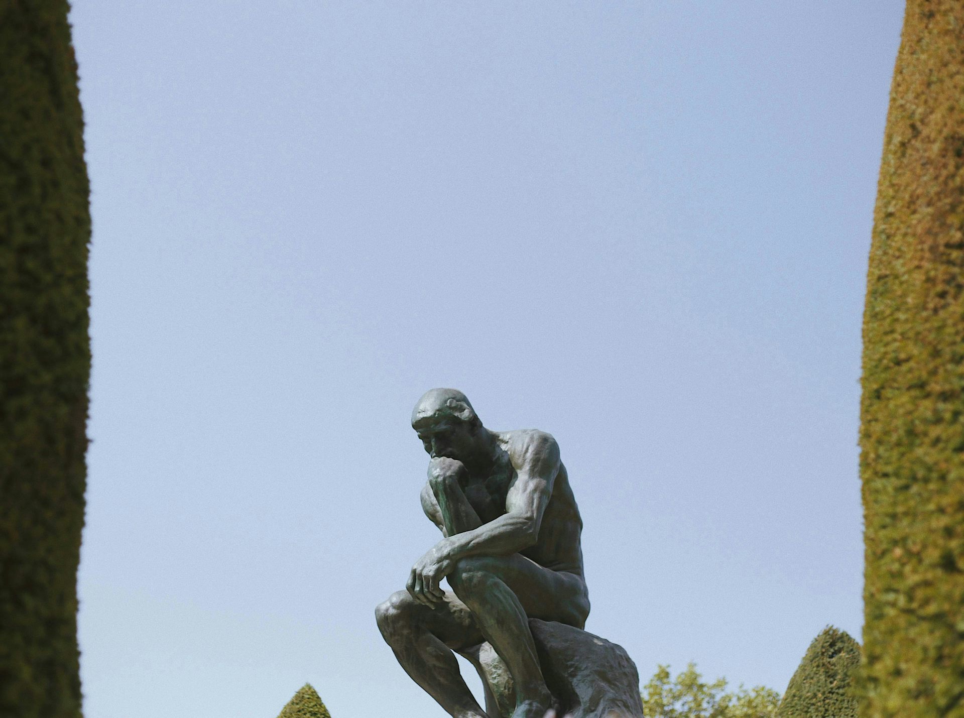 Le Penseur de Rodin, semblant perdu au milieu du ciel, et encadré par deux arbres sortant du champ de chaque côté.