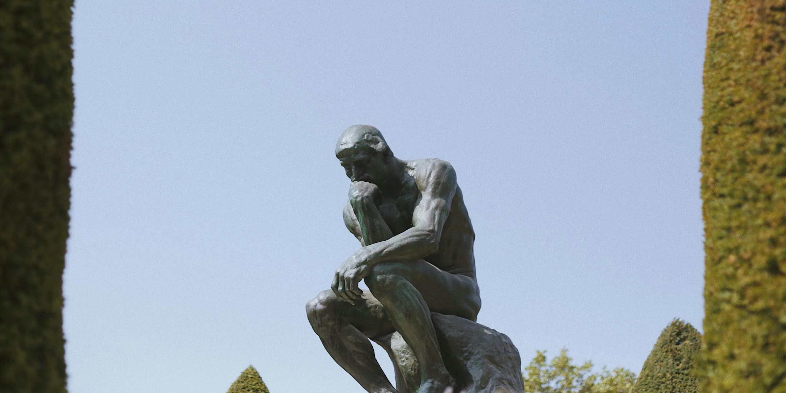 Le Penseur de Rodin, semblant perdu au milieu du ciel, et encadré par deux arbres sortant du champ de chaque côté.