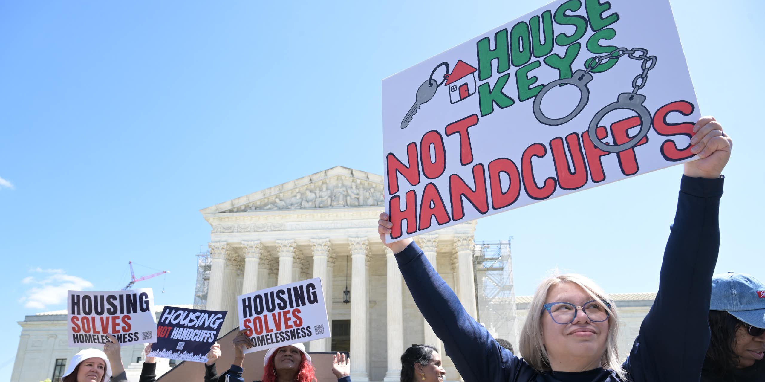 People hold signs reading 'House keys, not handcuffs' and 'Housing solves homelessness'