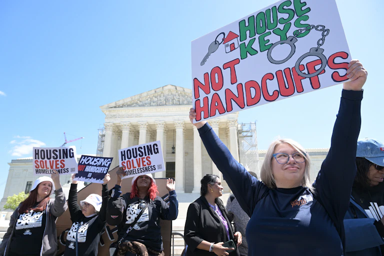 People hold signs reading 'House keys, not handcuffs' and 'Housing solves homelessness'