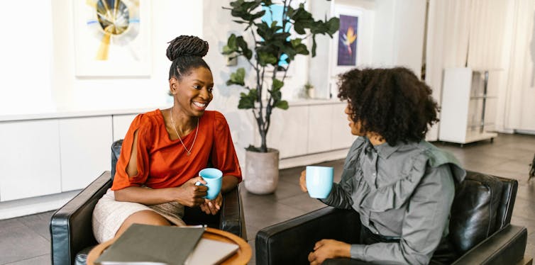 Two women with mugs and a laptop on a table in discussion.