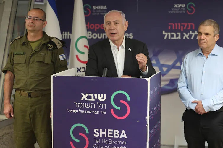 Israeli prime minister, Benjamin Netanyahu, speaks at a podium flanked by aides.
