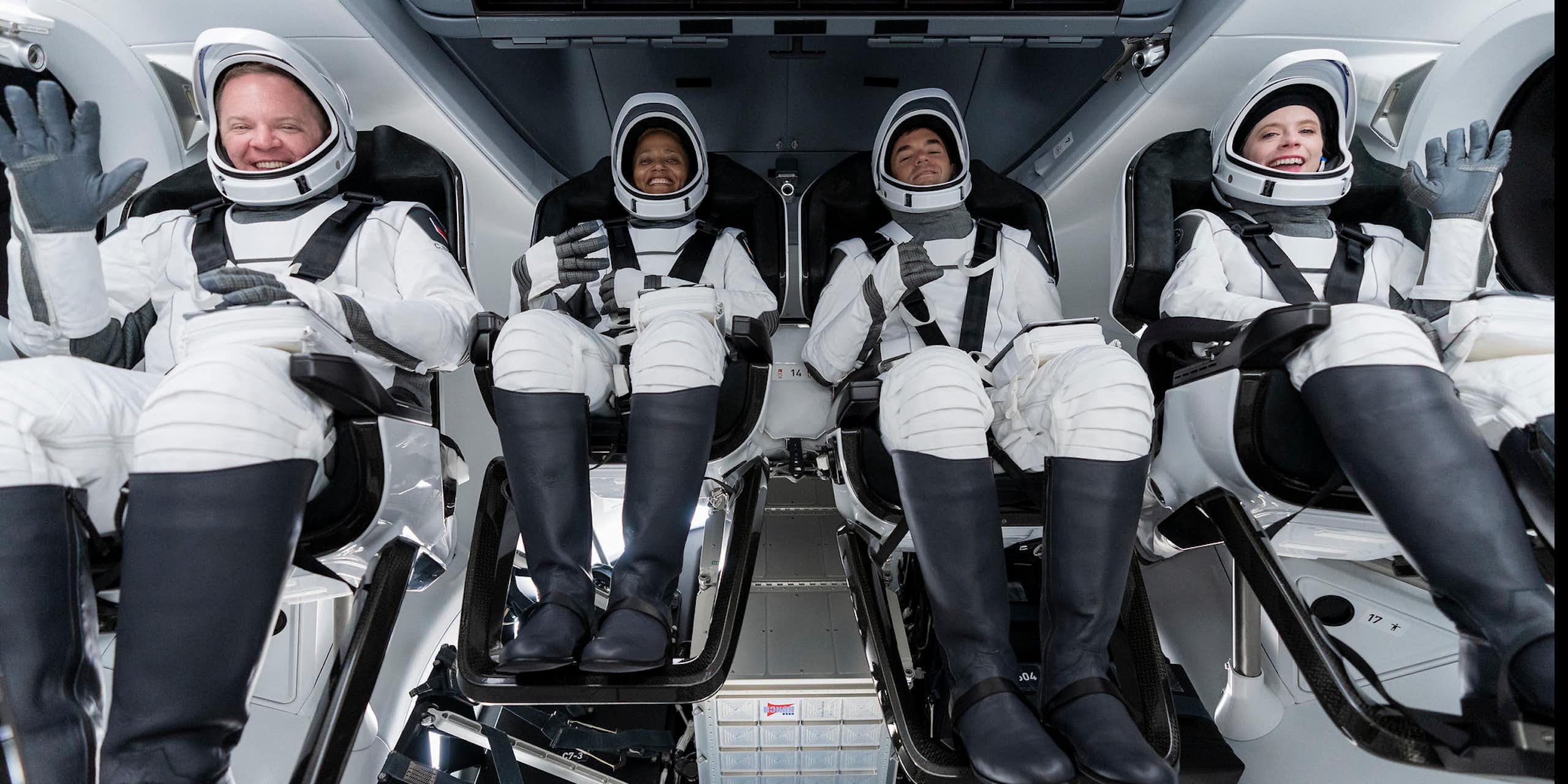 Four smiling people wearing white space suits.