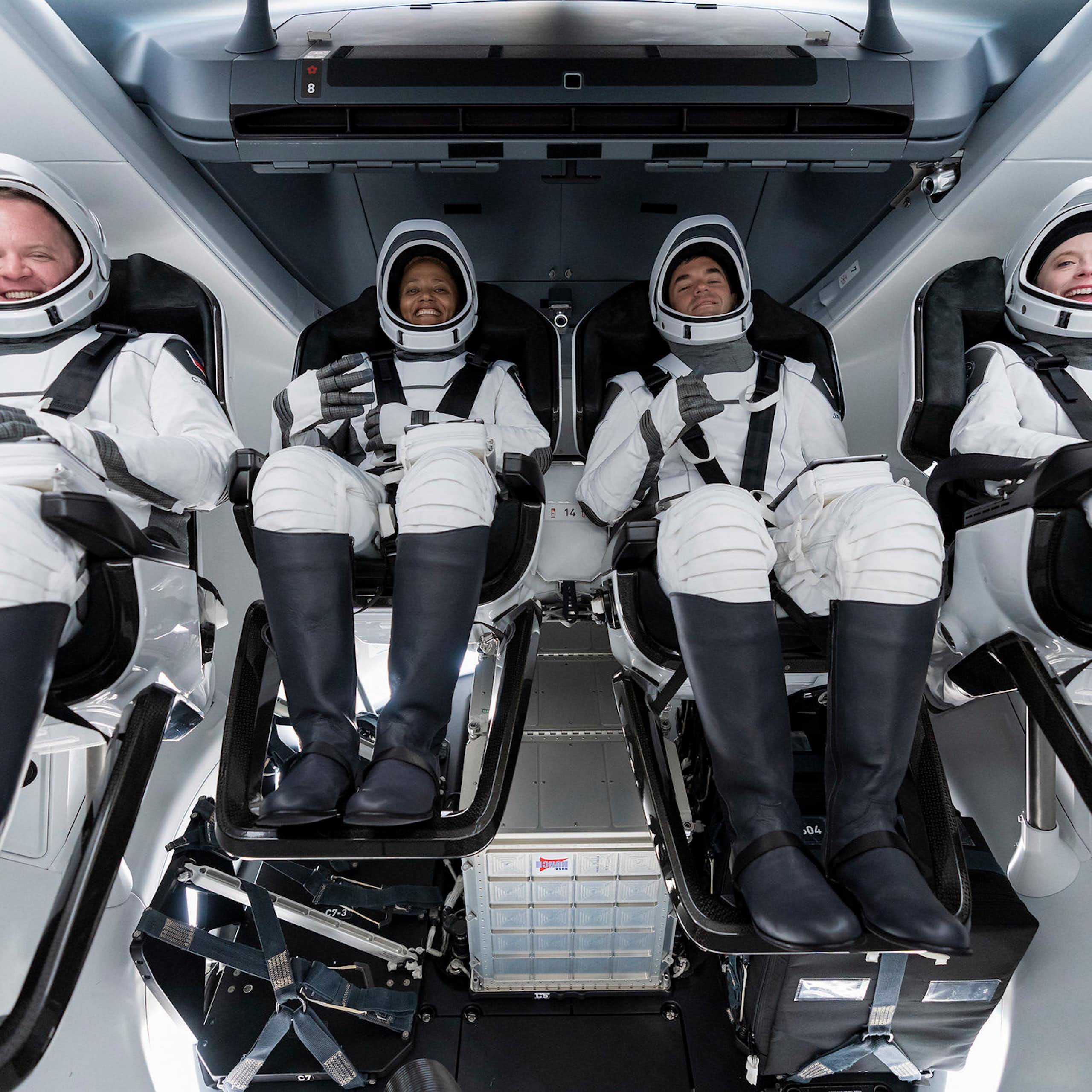 Four smiling people wearing white space suits.