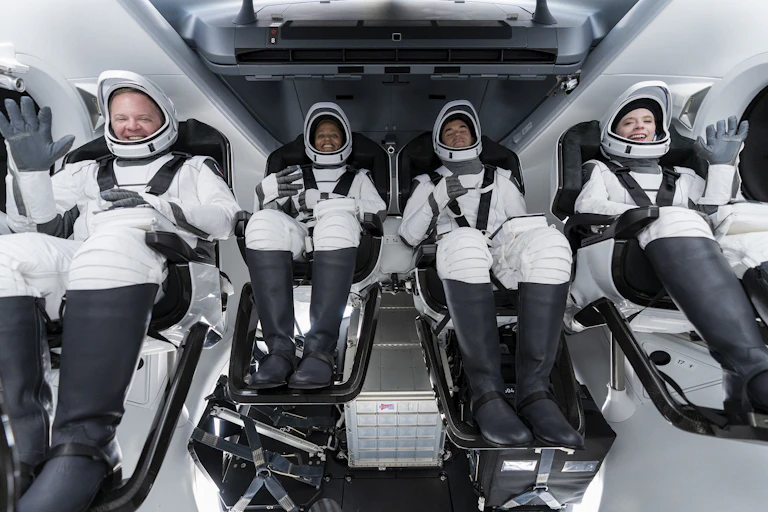 Four smiling people wearing white space suits.