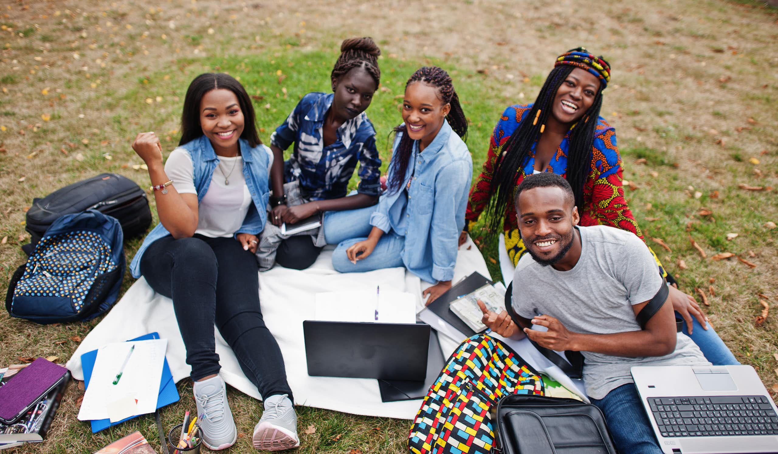 A group of Black students with laptops and knapsacks sitting outdoors.